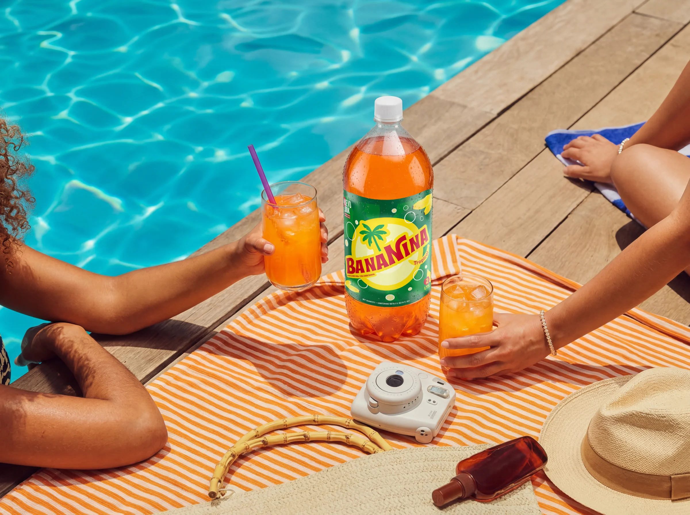 Botella y vasos de Bananina sobre una manta de picnic junto a una piscina